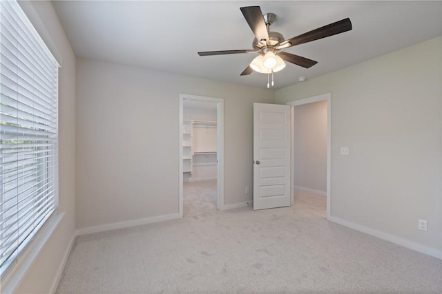 unfurnished bedroom featuring light carpet, a spacious closet, a closet, and baseboards