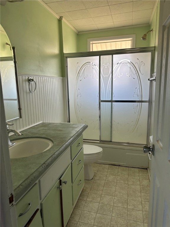 full bathroom with tile patterned flooring, bath / shower combo with glass door, toilet, and vanity