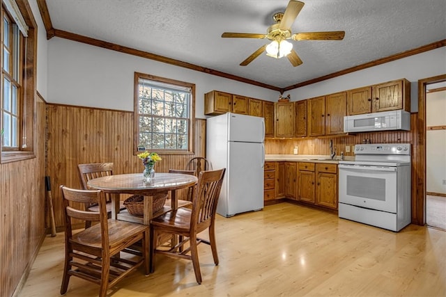 kitchen featuring a textured ceiling, white appliances, crown molding, light hardwood / wood-style flooring, and wood walls