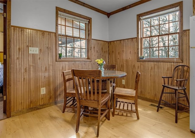 dining space featuring wooden walls, ornamental molding, and light wood-type flooring