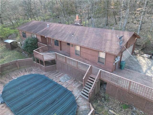 exterior space with a garage, roof with shingles, a wooden deck, and a view of trees