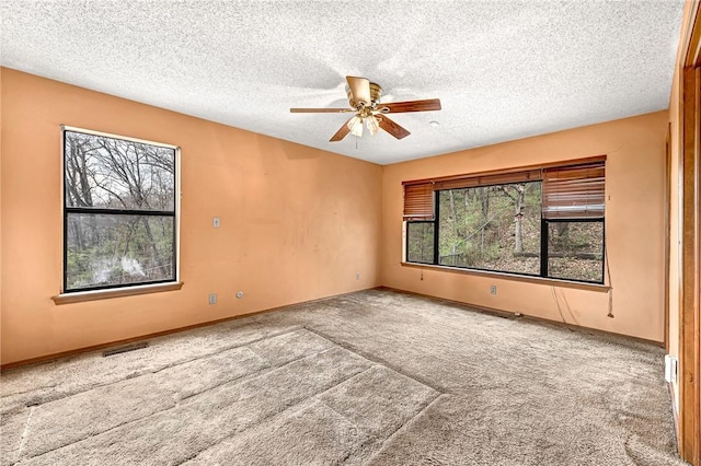 carpeted spare room with ceiling fan, a textured ceiling, visible vents, and baseboards