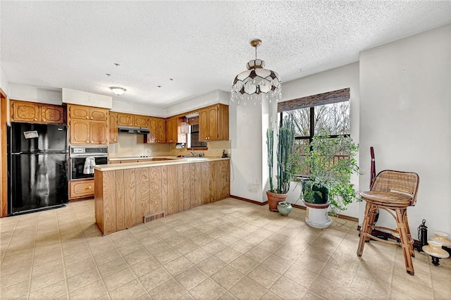 kitchen with under cabinet range hood, a peninsula, stainless steel oven, light countertops, and freestanding refrigerator