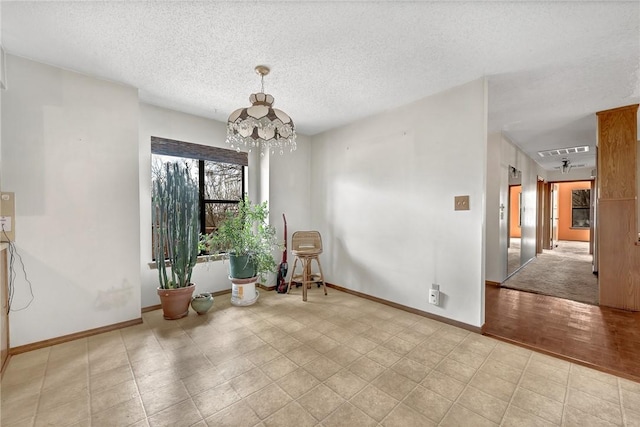 unfurnished room with a chandelier, a textured ceiling, visible vents, and baseboards