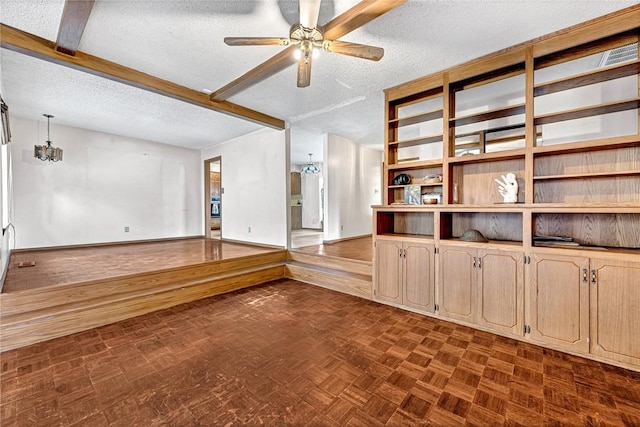 spare room with a textured ceiling, ceiling fan with notable chandelier, beam ceiling, and baseboards