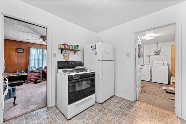 kitchen featuring washing machine and clothes dryer, ceiling fan, wooden walls, white appliances, and light carpet