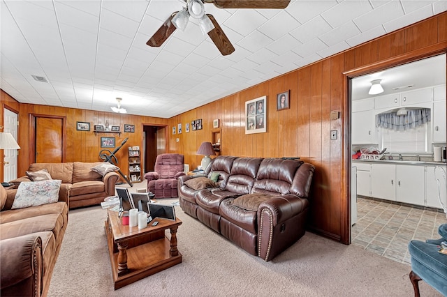 carpeted living room with wooden walls and ceiling fan