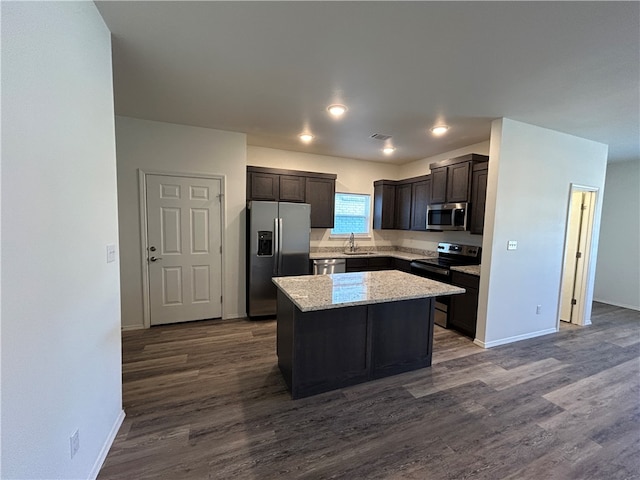 kitchen with light stone counters, dark hardwood / wood-style floors, stainless steel appliances, a center island, and sink