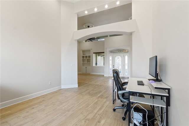 home office with a high ceiling, light hardwood / wood-style floors, and french doors