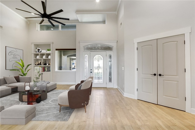 living room with light wood-type flooring, ceiling fan, a high ceiling, and crown molding