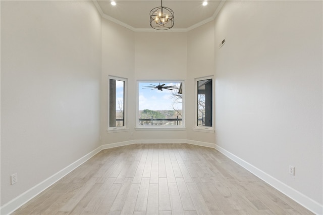 empty room with ornamental molding, a towering ceiling, light hardwood / wood-style floors, and a notable chandelier