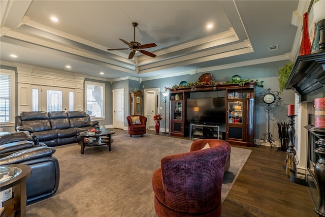 living room with ceiling fan, crown molding, a fireplace, dark wood-type flooring, and a tray ceiling