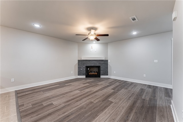 unfurnished living room featuring ceiling fan, hardwood / wood-style floors, and a stone fireplace