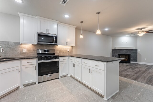 kitchen with pendant lighting, ceiling fan, stainless steel appliances, a stone fireplace, and light wood-type flooring