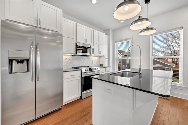 kitchen featuring appliances with stainless steel finishes, light wood-type flooring, white cabinets, and an island with sink