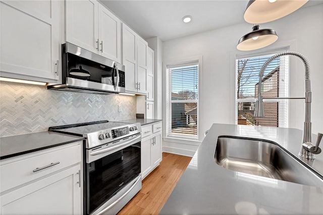 kitchen with tasteful backsplash, dark countertops, appliances with stainless steel finishes, light wood-style floors, and a sink