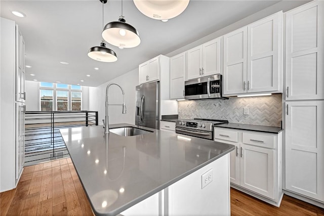 kitchen featuring dark countertops, decorative backsplash, white cabinets, stainless steel appliances, and a sink