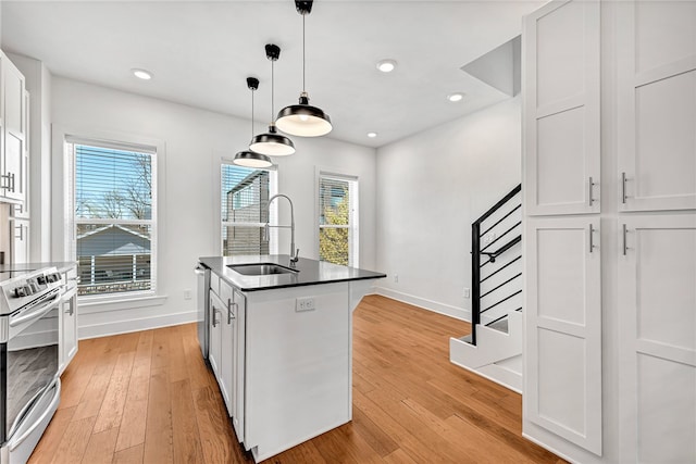 kitchen featuring white cabinets, appliances with stainless steel finishes, decorative light fixtures, sink, and a kitchen island with sink