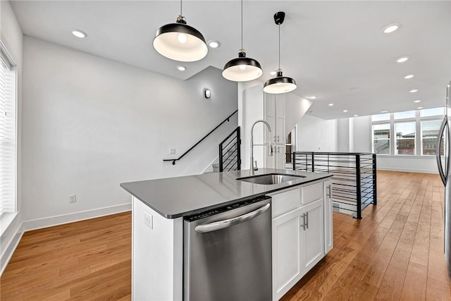 kitchen with a sink, stainless steel dishwasher, dark countertops, and light wood-style flooring