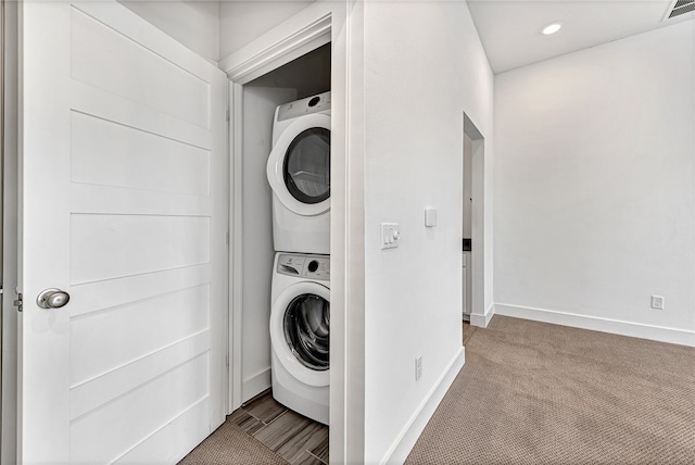 clothes washing area featuring stacked washing maching and dryer and light carpet