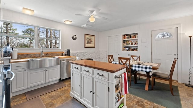 kitchen with built in shelves, ceiling fan, sink, stainless steel dishwasher, and white cabinets