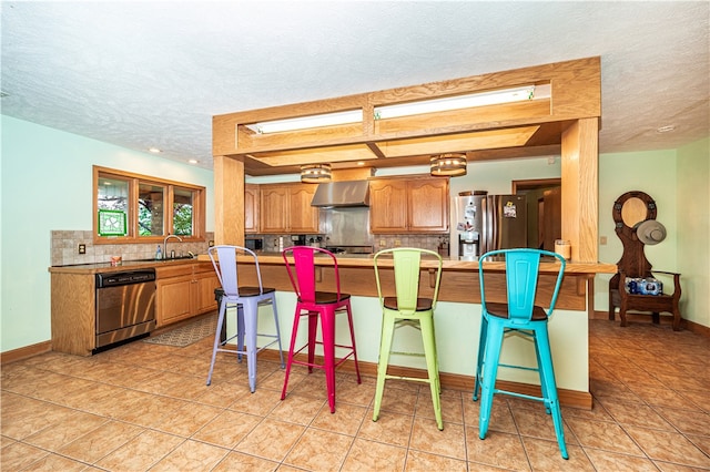 kitchen featuring a textured ceiling, appliances with stainless steel finishes, wall chimney exhaust hood, tasteful backsplash, and light tile flooring