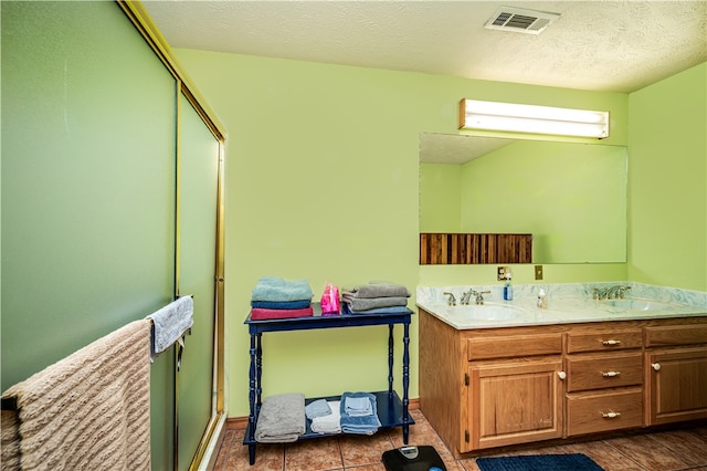 bathroom with vanity with extensive cabinet space, double sink, a textured ceiling, and tile floors