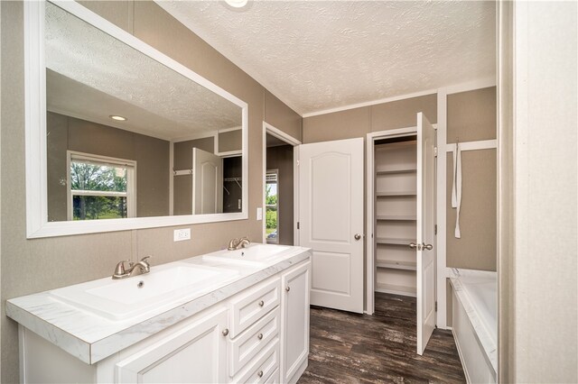 bathroom with a textured ceiling, double sink, a bath to relax in, wood-type flooring, and oversized vanity