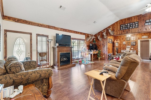 living room featuring wood walls, lofted ceiling, ceiling fan, and dark wood-type flooring