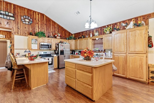 kitchen with an inviting chandelier, appliances with stainless steel finishes, light hardwood / wood-style floors, a center island, and vaulted ceiling