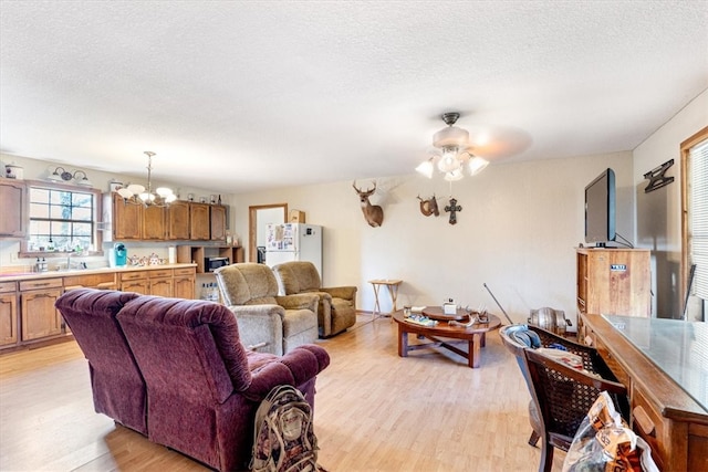 living room with a textured ceiling, ceiling fan with notable chandelier, and light wood-type flooring