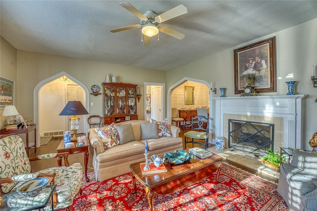 living room featuring a tiled fireplace, a textured ceiling, wood-type flooring, and ceiling fan