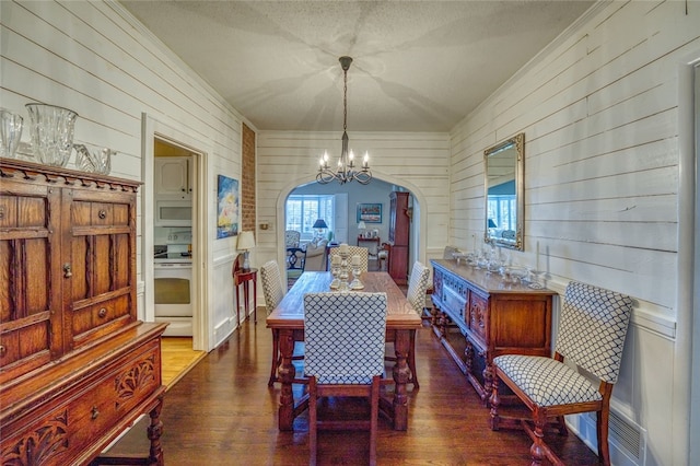 dining area with an inviting chandelier, dark hardwood / wood-style flooring, a textured ceiling, and wood walls