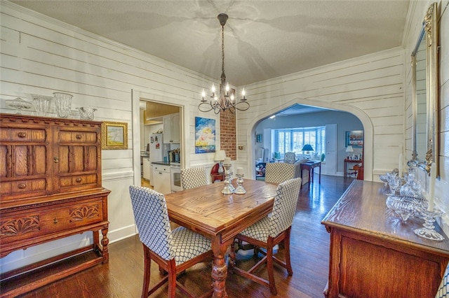 dining area with wooden walls, a textured ceiling, a notable chandelier, and dark wood-type flooring