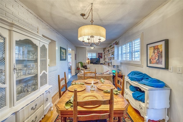 dining space with an inviting chandelier, a textured ceiling, brick wall, and light hardwood / wood-style flooring