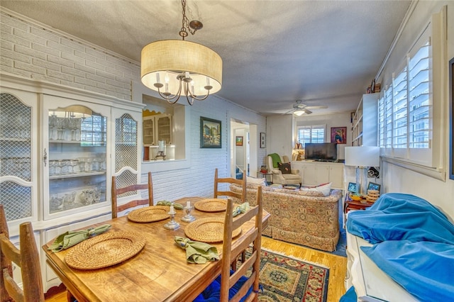 dining area with brick wall, ornamental molding, and ceiling fan with notable chandelier