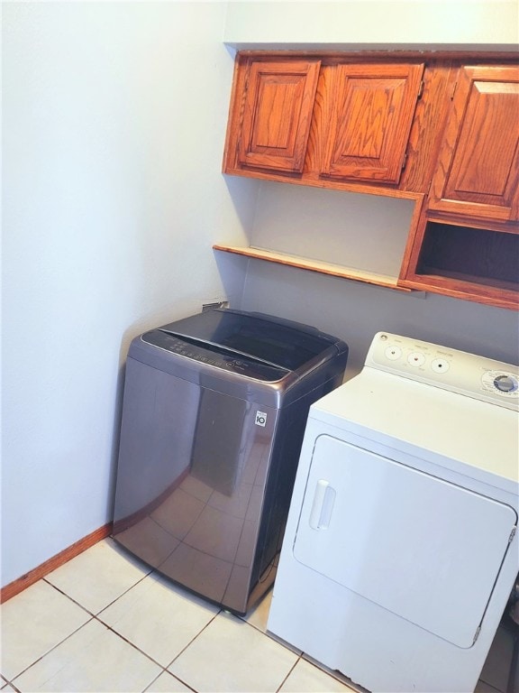 laundry area featuring washing machine and clothes dryer, cabinets, and light tile floors