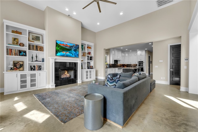 living room with built in features, a towering ceiling, ceiling fan, and a fireplace