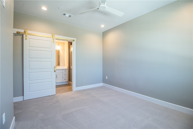 unfurnished bedroom with ensuite bath, ceiling fan, light tile floors, and a barn door