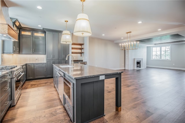 kitchen with an island with sink, pendant lighting, light hardwood / wood-style floors, and high end range