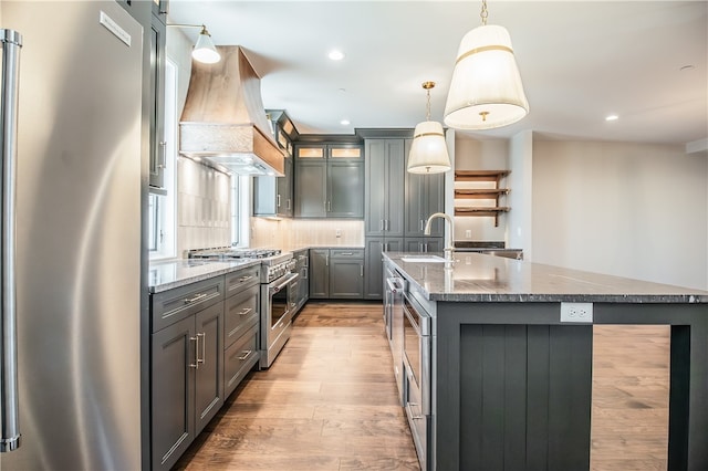 kitchen with backsplash, light hardwood / wood-style flooring, custom range hood, high quality appliances, and pendant lighting