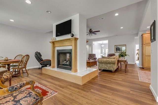 living room featuring a premium fireplace, wood-type flooring, and ceiling fan