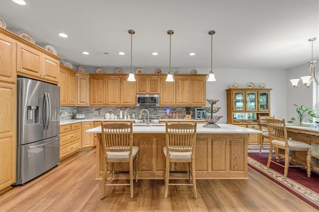 kitchen with backsplash, light wood-type flooring, stainless steel appliances, an island with sink, and pendant lighting