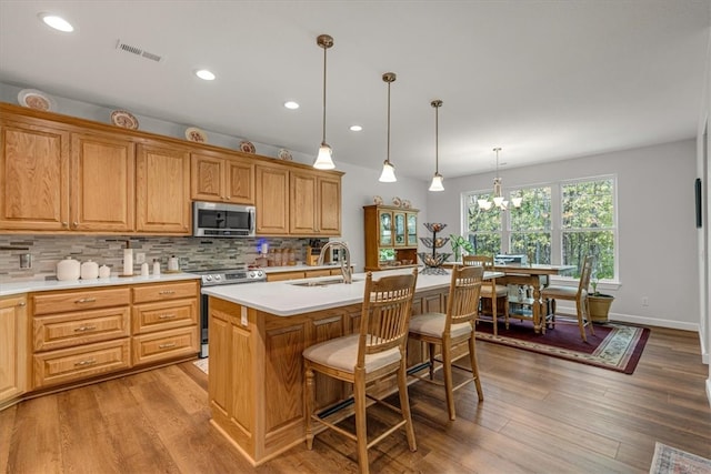 kitchen with backsplash, hardwood / wood-style flooring, a kitchen island with sink, and range