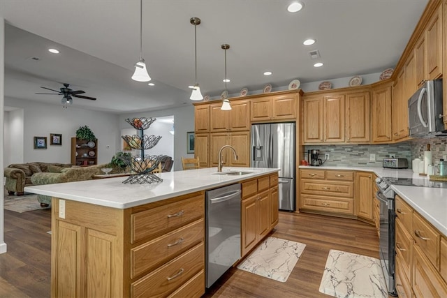 kitchen with appliances with stainless steel finishes, ceiling fan, a center island with sink, tasteful backsplash, and hardwood / wood-style flooring