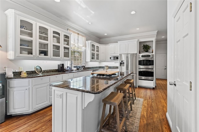 kitchen with appliances with stainless steel finishes, a kitchen island, white cabinets, ornamental molding, and wood-type flooring