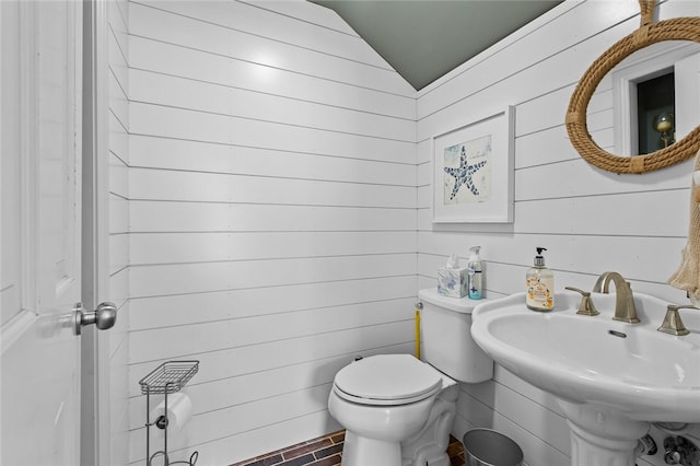 bathroom with vaulted ceiling, wood walls, sink, and toilet