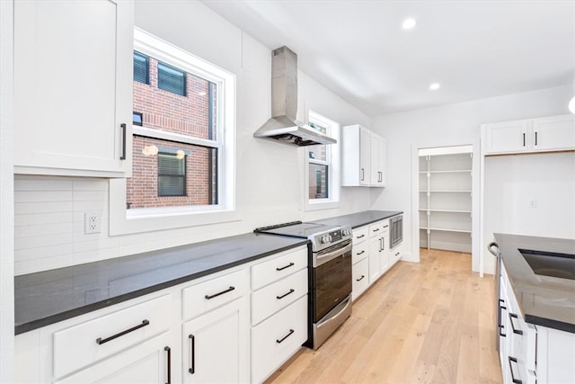 kitchen with stainless steel appliances, light hardwood / wood-style floors, wall chimney range hood, and white cabinetry