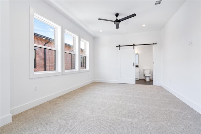 unfurnished bedroom with ensuite bath, carpet floors, ceiling fan, and a barn door