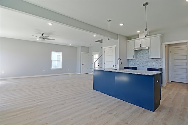 kitchen with hanging light fixtures, white cabinets, backsplash, sink, and light hardwood / wood-style floors